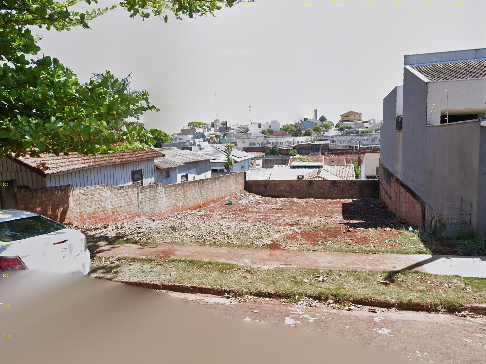 Vista do Street View de 2025: lote de terra vazio, muro de tijolo à esquerda, sobrado cinza à direita e a cidade mais baixa ao fundo